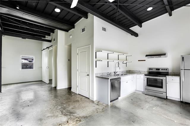 kitchen featuring sink, appliances with stainless steel finishes, a barn door, high vaulted ceiling, and white cabinetry