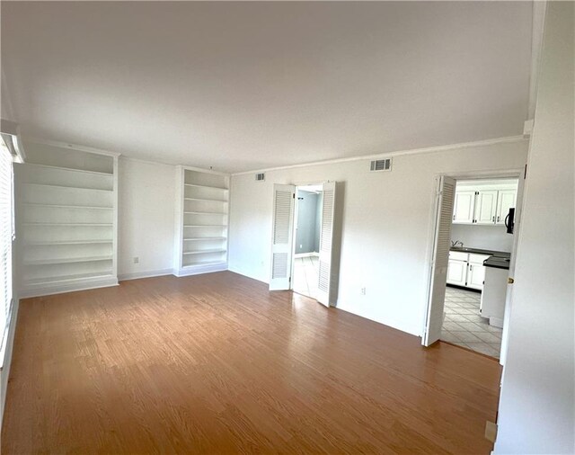 interior space with built in shelves, ornamental molding, wood finished floors, and visible vents