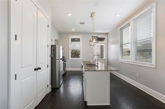 kitchen featuring plenty of natural light, dark wood-type flooring, stainless steel fridge, sink, and pendant lighting