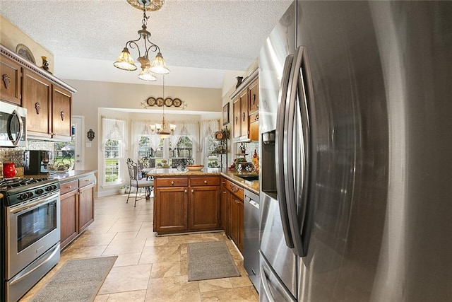 kitchen with stainless steel appliances, hanging light fixtures, kitchen peninsula, an inviting chandelier, and light tile patterned floors