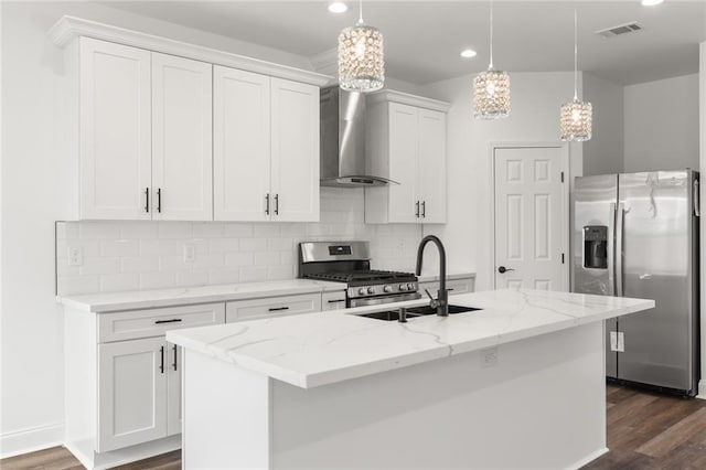 kitchen featuring appliances with stainless steel finishes, a center island with sink, white cabinetry, backsplash, and wall chimney range hood