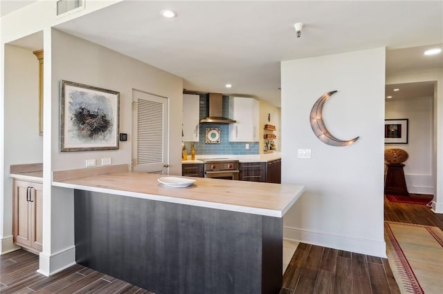 kitchen featuring wall chimney exhaust hood, white cabinetry, decorative backsplash, and kitchen peninsula