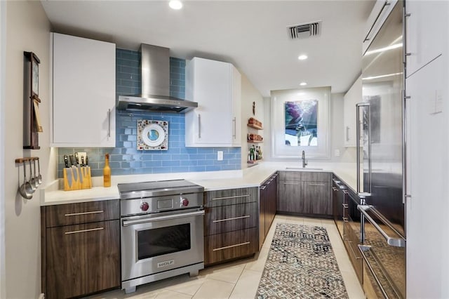 kitchen with high quality appliances, white cabinets, dark brown cabinets, wall chimney range hood, and sink