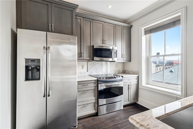 kitchen with light stone counters, dark hardwood / wood-style flooring, ornamental molding, and appliances with stainless steel finishes