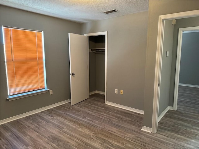 unfurnished bedroom featuring a closet, a textured ceiling, and dark hardwood / wood-style flooring