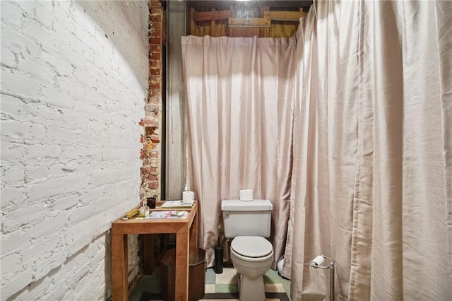 bathroom featuring brick wall and toilet