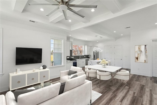 living room featuring dark hardwood / wood-style flooring, coffered ceiling, ceiling fan with notable chandelier, sink, and beam ceiling