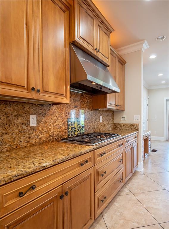 kitchen featuring light tile patterned floors, backsplash, ornamental molding, light stone countertops, and stainless steel gas cooktop