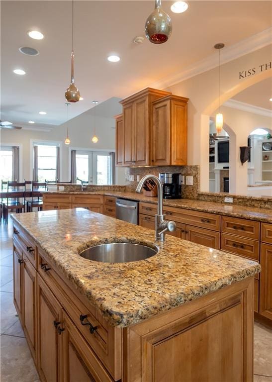 kitchen with pendant lighting, decorative backsplash, a kitchen island with sink, light stone counters, and kitchen peninsula