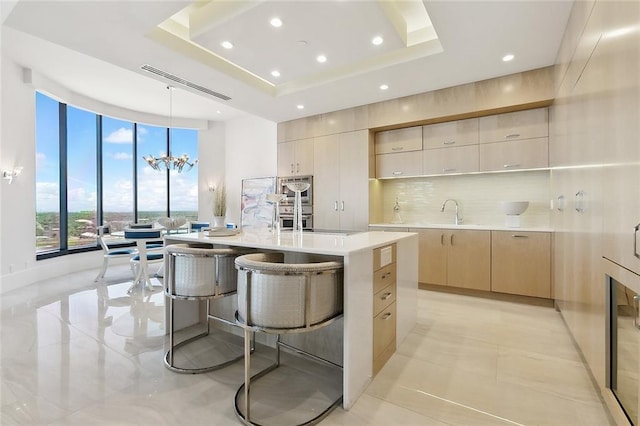 kitchen with decorative light fixtures, a notable chandelier, an island with sink, light tile floors, and a raised ceiling