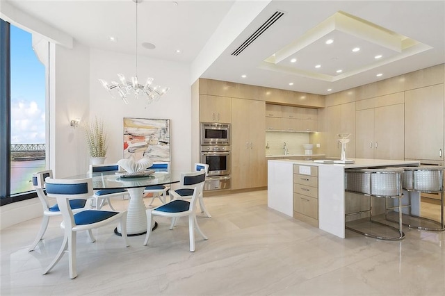 kitchen with an island with sink, light brown cabinetry, hanging light fixtures, and a chandelier