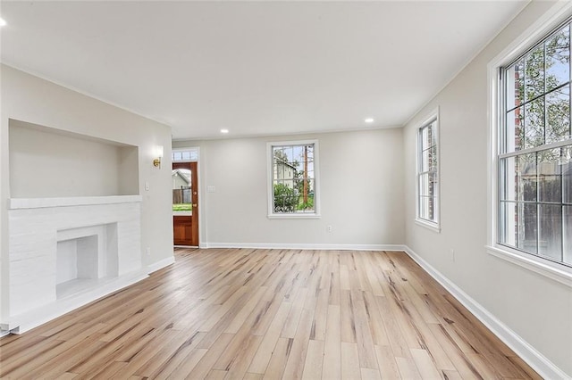 unfurnished living room with plenty of natural light, built in features, a brick fireplace, and light hardwood / wood-style flooring