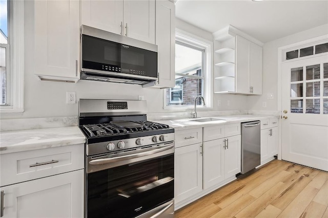 kitchen with light hardwood / wood-style flooring, appliances with stainless steel finishes, sink, white cabinets, and light stone counters