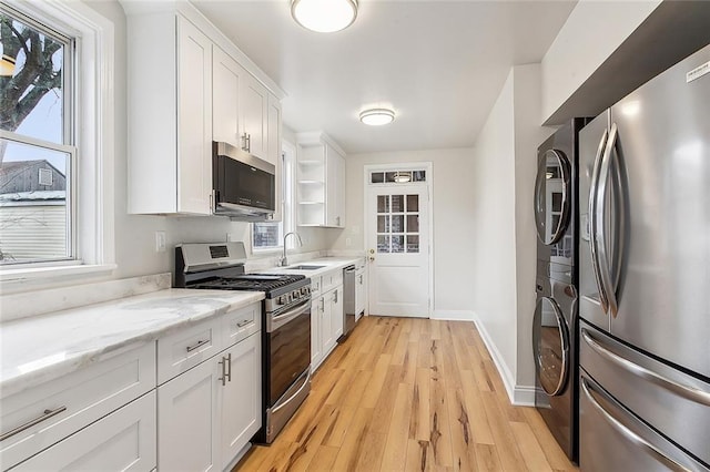 kitchen with plenty of natural light, white cabinets, appliances with stainless steel finishes, light stone countertops, and light wood-type flooring