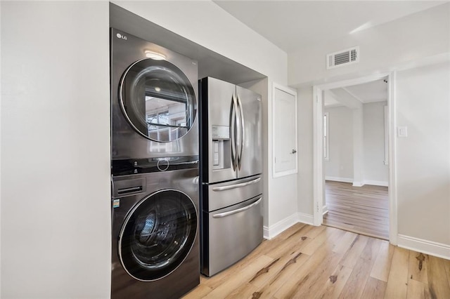 laundry area with stacked washer / drying machine and light wood-type flooring