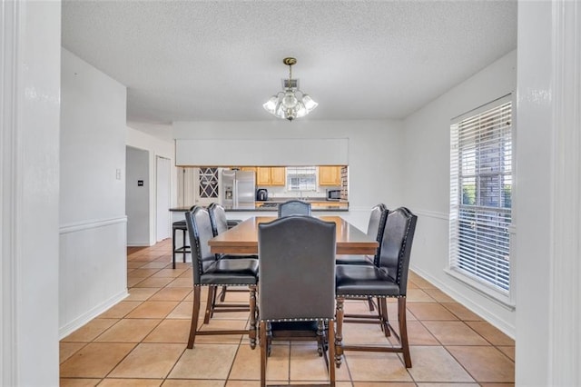 dining area with light tile floors, a textured ceiling, and an inviting chandelier