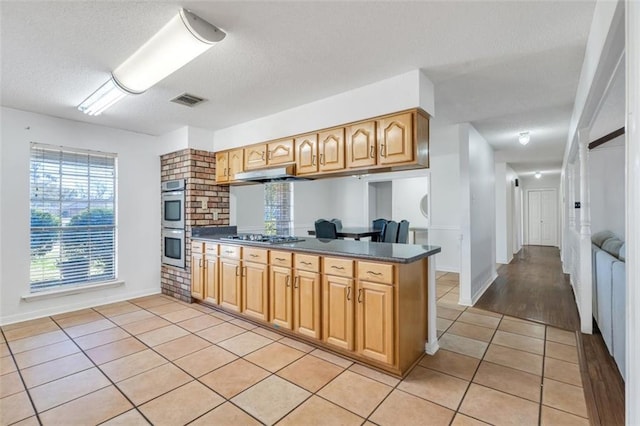 kitchen with light tile flooring, stainless steel appliances, kitchen peninsula, and a textured ceiling