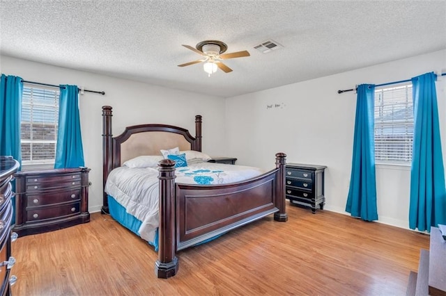 bedroom featuring ceiling fan, a textured ceiling, multiple windows, and light hardwood / wood-style floors