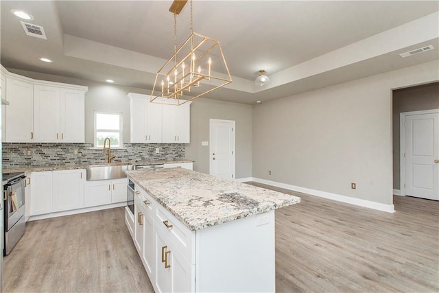 kitchen featuring sink, light wood-type flooring, a center island, white cabinets, and stove