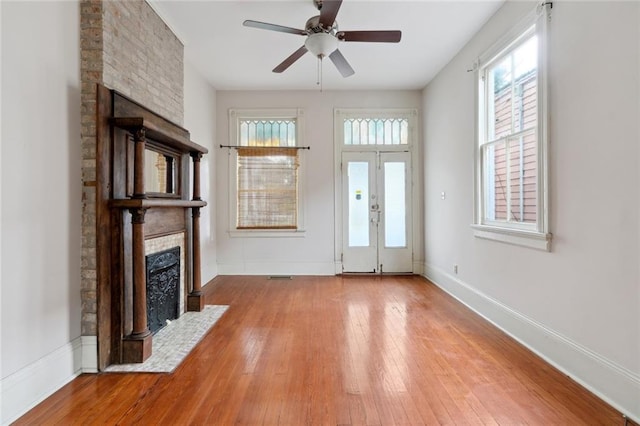 unfurnished living room featuring light hardwood / wood-style flooring, ceiling fan, a fireplace, and french doors