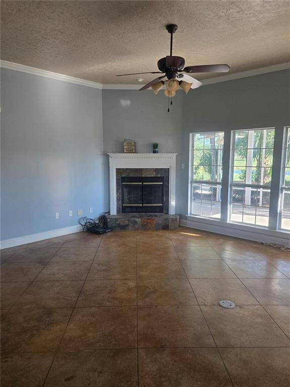 unfurnished living room featuring a stone fireplace, a textured ceiling, ceiling fan, dark tile patterned floors, and ornamental molding