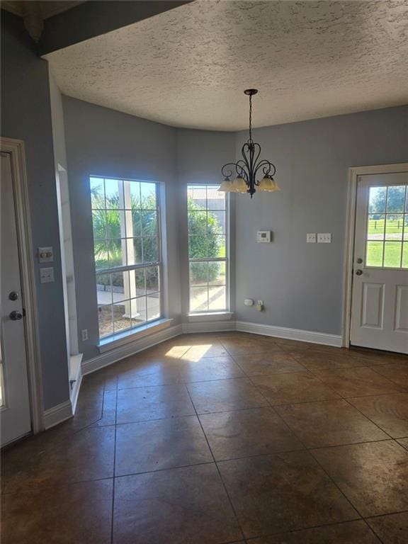 unfurnished dining area with an inviting chandelier, dark tile patterned flooring, plenty of natural light, and a textured ceiling