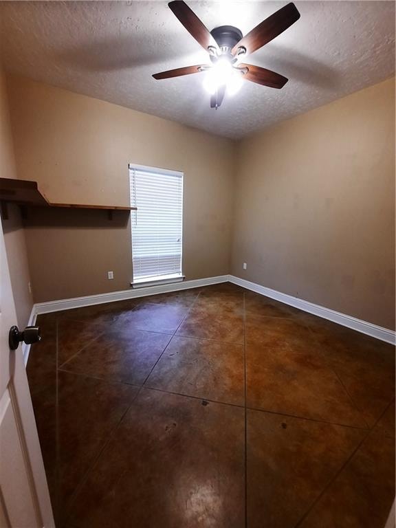 empty room with a textured ceiling, ceiling fan, and dark tile patterned flooring