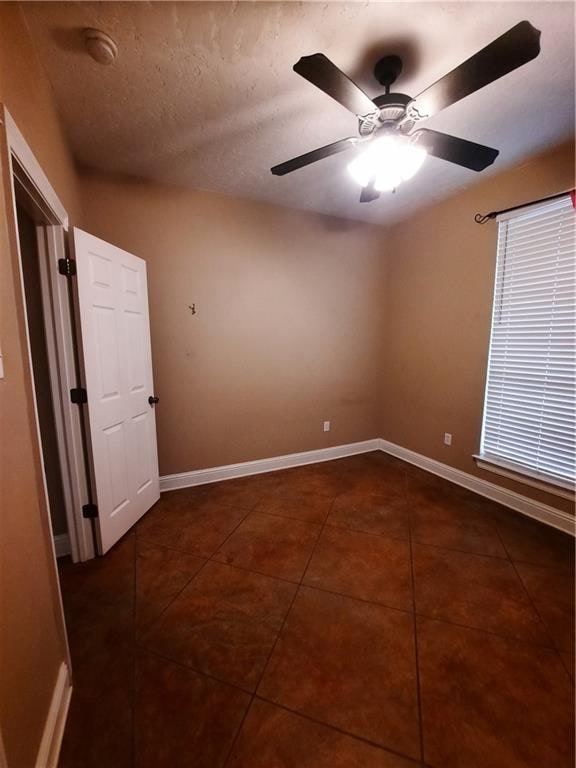 tiled empty room featuring ceiling fan and a textured ceiling