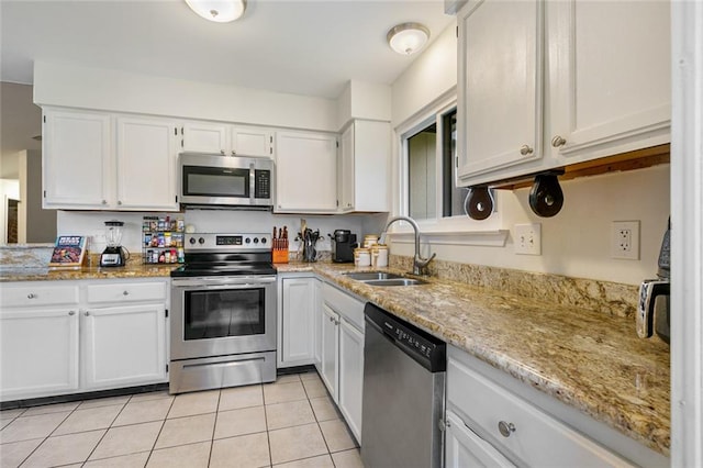 kitchen featuring appliances with stainless steel finishes, light stone counters, white cabinets, light tile floors, and sink