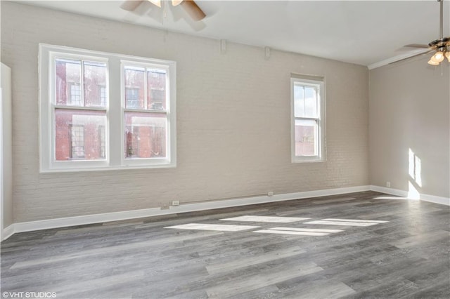 spare room featuring plenty of natural light, dark hardwood / wood-style floors, ceiling fan, and brick wall