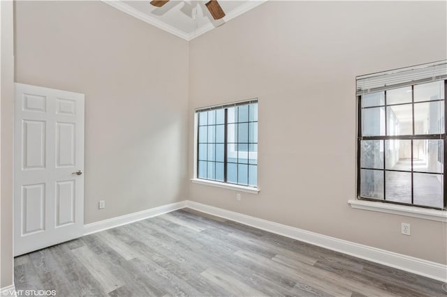 empty room with ornamental molding, ceiling fan, a towering ceiling, and light hardwood / wood-style flooring