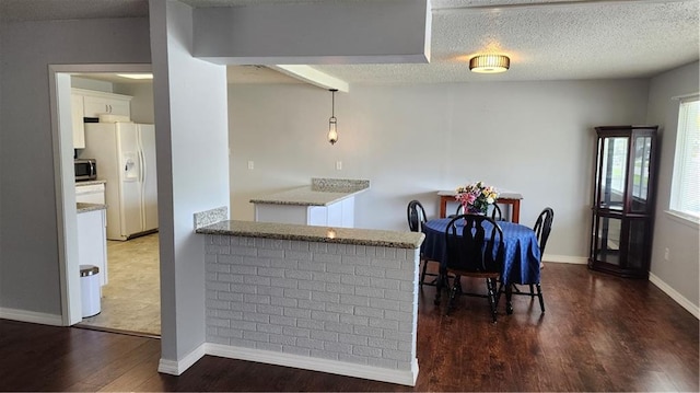 kitchen with a textured ceiling, white fridge with ice dispenser, dark hardwood / wood-style flooring, and white cabinets