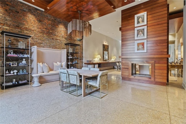 living room featuring wooden ceiling, a fireplace, a towering ceiling, and brick wall