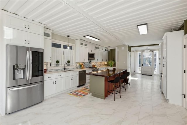 kitchen featuring sink, a kitchen island, a kitchen breakfast bar, white cabinets, and appliances with stainless steel finishes