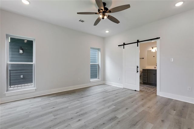 unfurnished bedroom featuring light hardwood / wood-style flooring, ceiling fan, ensuite bathroom, and a barn door