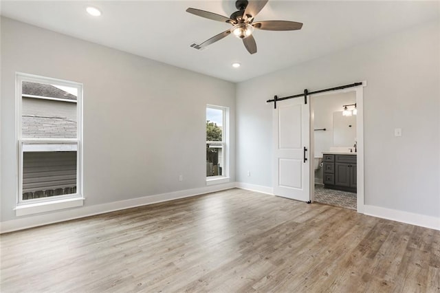 unfurnished bedroom with ensuite bathroom, a barn door, ceiling fan, hardwood / wood-style flooring, and sink