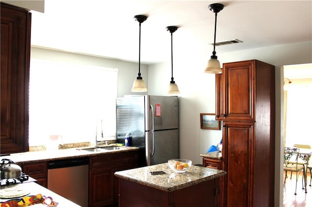 kitchen featuring light stone counters, stainless steel appliances, hanging light fixtures, sink, and a center island