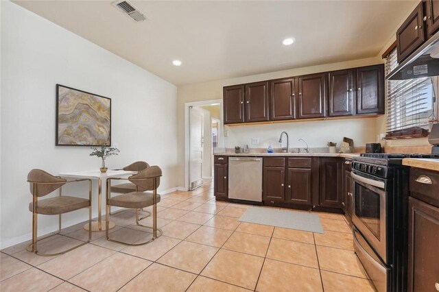 kitchen featuring range with gas stovetop, stainless steel dishwasher, dark brown cabinets, and light tile patterned flooring