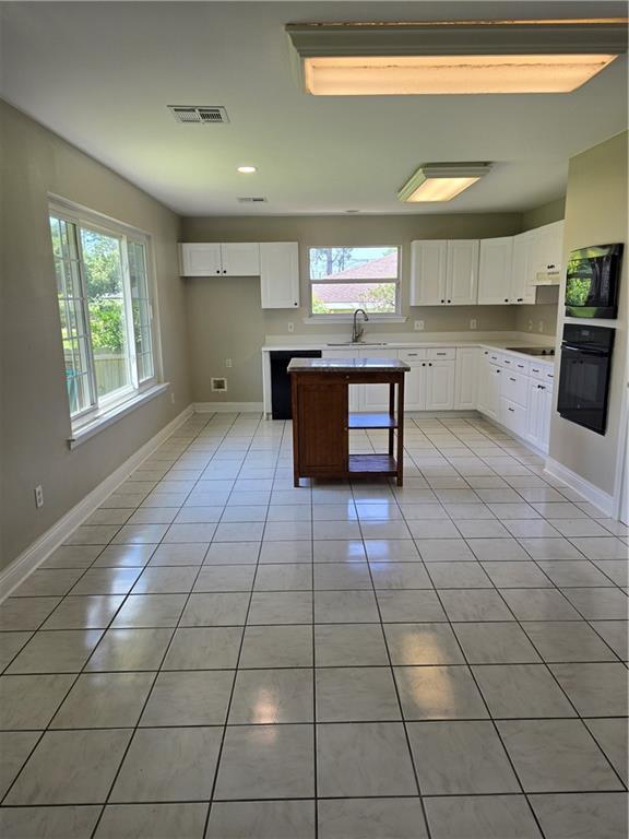 kitchen featuring sink, white cabinets, a center island, light tile patterned floors, and black appliances