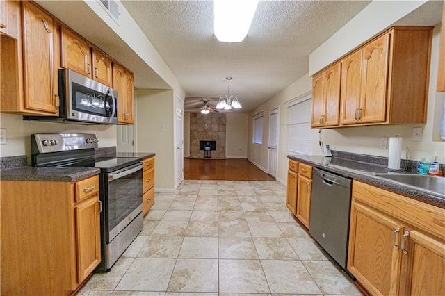 kitchen featuring decorative light fixtures, ceiling fan, stainless steel appliances, a textured ceiling, and light wood-type flooring