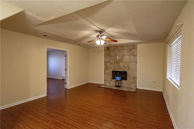 unfurnished living room with tile walls, ceiling fan, a tiled fireplace, a textured ceiling, and dark hardwood / wood-style flooring