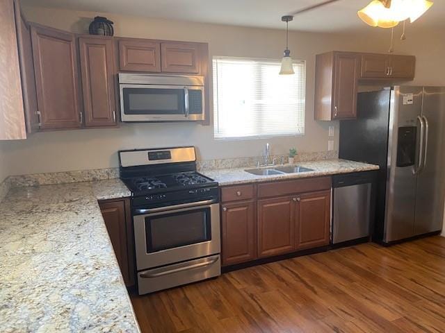 kitchen featuring appliances with stainless steel finishes, dark wood-type flooring, light stone counters, decorative light fixtures, and sink