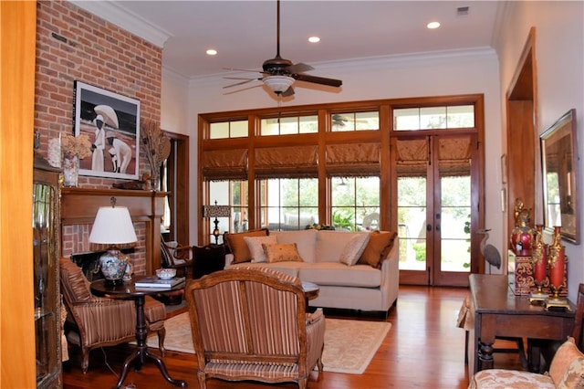 living room featuring wood-type flooring, ceiling fan, a fireplace, ornamental molding, and french doors