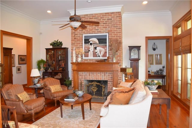 living room with brick wall, a brick fireplace, ceiling fan, dark wood-type flooring, and crown molding