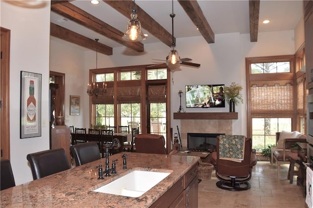 interior space with a tiled fireplace, decorative light fixtures, ceiling fan, a healthy amount of sunlight, and light stone counters