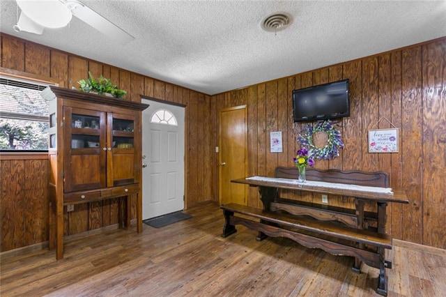 foyer with ceiling fan, wood walls, dark hardwood / wood-style floors, and a textured ceiling