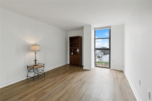 spare room featuring a wall of windows, wood finished floors, and baseboards