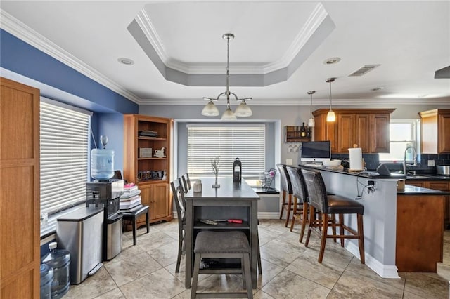 kitchen featuring ornamental molding, decorative light fixtures, light tile floors, and a raised ceiling