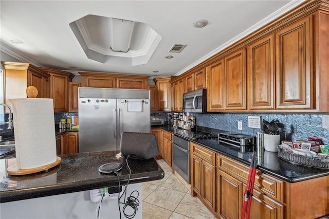 kitchen featuring ornamental molding, stainless steel appliances, a raised ceiling, tasteful backsplash, and dark stone countertops