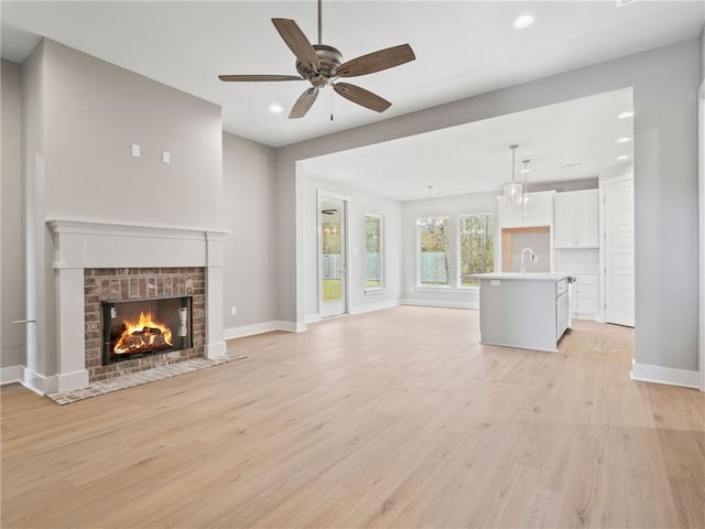 unfurnished living room with ceiling fan, a brick fireplace, sink, and light wood-type flooring